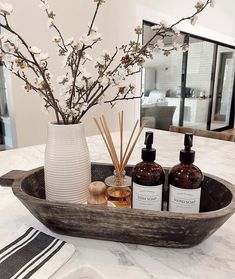 a wooden tray with bottles and flowers in it sitting on a marble counter top next to a mirror