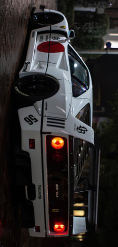 the back end of a white race car with its lights on and taillights turned red