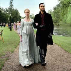 a man and woman dressed in period clothing walking down a path