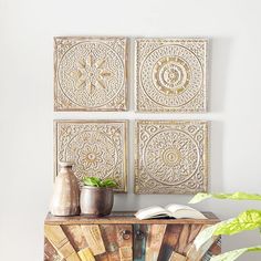 three metal wall art pieces on top of a wooden table next to a potted plant