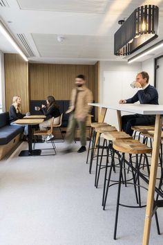 people are sitting at tables in an office with chairs and desks, while one man walks by