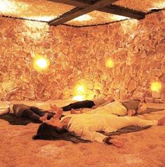 three people laying on the ground in front of a stone wall with lights hanging from it