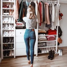 a woman standing in front of a closet full of clothes and shoes, looking into the closet