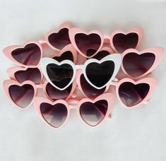 pink heart shaped sunglasses with white frames and black lenses on a white tablecloth background