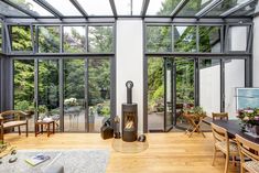 a living room filled with furniture and lots of glass walls covered in plants on top of wooden flooring