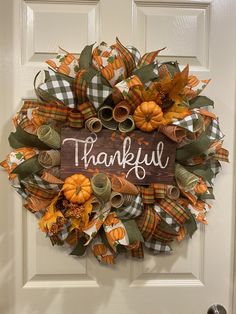 a wreath with the words, happy thanksgiving written on it and pumpkins hanging from the front door