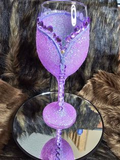 a purple wine glass sitting on top of a table next to a round mirror and fur