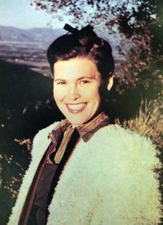 an old photo of a woman wearing a coat and smiling at the camera with trees in the background