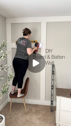 a woman is standing on a chair and using a drill to fix the wall in her living room