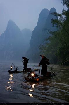 two people on small boats in the water with mountains in the backgrouds