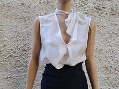 This ivory white sleeveless blouse is essential to any well-edited wardrobe. Laid back yet chic, it's crafted in 100% pure silk with a pleat relaxed shape and flattering / boat neckline. Perfect for event, work or off-duty dressing it will take you through the new season and beyond. * Measurements: Size S  Bust :50 cm ( 20'' in)- laying flat measured from one armpit to the other. Hips :54 ( 21'' in) Long : 56 cm ( 22'' in)- length measurement is taken from top of the front shoulder to hem. Size Elegant V-neck Top With Bow, Elegant V-neck Blouse For Summer, Elegant Party Top With Bow, Elegant Sleeveless Blouse With Bow, Chic Sleeveless Blouse For Office, Chic Sleeveless Office Blouse, Feminine Party Blouse With Bow, White Tie Neck Blouse For Formal Occasions, Feminine Office Tops With Bow Detail