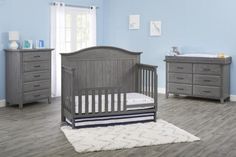 a baby's room with blue walls and gray furniture, including a crib