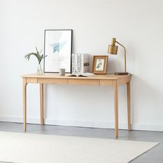 a wooden table sitting in front of a white wall next to a lamp and pictures