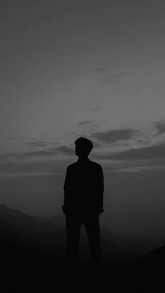 a man standing on top of a hill under a dark sky with clouds in the background