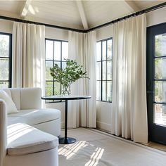 a living room filled with white furniture and windows covered in drapes next to a table