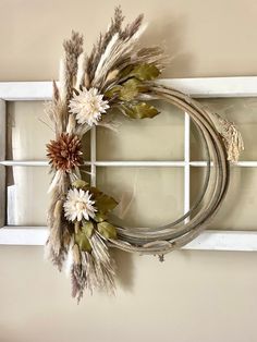 a wreath with dried flowers hanging on a window sill