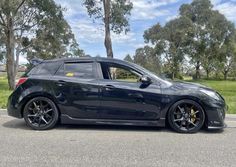 a black car is parked on the side of the road in front of some trees