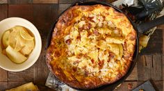 a pizza with cheese and potatoes in a pan next to a bowl of sliced apples