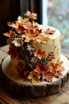 there is a cake decorated with fall leaves on the wooden table next to a window