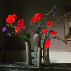 three vases with flowers in them sitting on a shelf