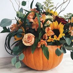 a pumpkin filled with lots of flowers and greenery