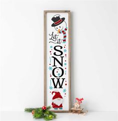 a wooden sign with the words let it snow and a christmas decoration on top of it