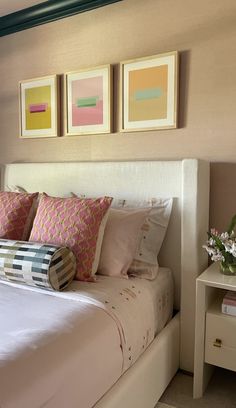 a white bed topped with lots of pillows next to two framed pictures on the wall