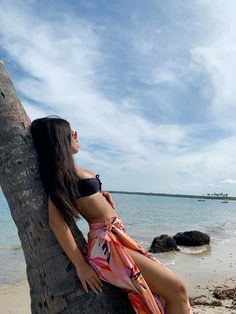 a woman sitting on top of a palm tree next to the ocean