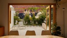 a table and chairs in front of an open patio door with potted plants on either side