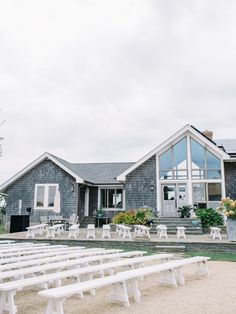 several white benches in front of a gray house with flowers on the porch and windows