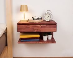 a wooden shelf with books and an alarm clock on it next to a bed in a bedroom