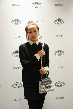 a woman holding a purse in front of a white wall with the word deucee on it