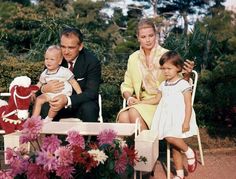 two adults and two children sitting on chairs with flowers in the foreground, one holding a baby