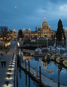 boats are docked in the water at night near a large building with lights on it