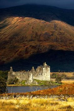 an old castle sitting in the middle of a field next to a large mountain range