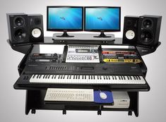 there is a keyboard and two monitors on the desk with music equipment in front of it