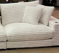 a white couch covered in lots of pillows on top of a carpeted room floor