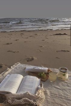 an open book sitting on top of a sandy beach next to the ocean with food