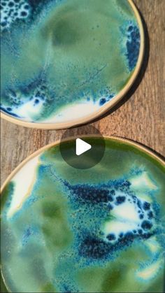 two plates with blue and green designs on them sitting on a wooden table next to each other