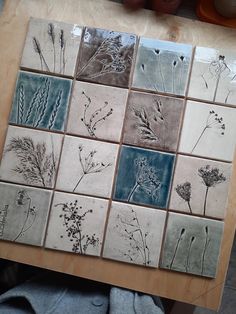 a wooden table topped with lots of tiles covered in different types of flowers and plants