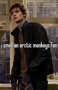 a man in a black jacket and tie standing next to a window with the words i smell an arctic monkeys fan