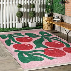 a pink rug with green and red flowers on it in front of a white fence