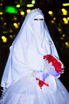 a woman in a white veil and dress with flowers on her wedding day at night