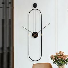 a clock mounted to the side of a wall next to a chair and vase with flowers