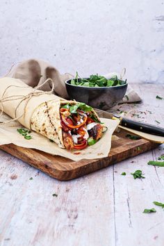 a pita sandwich on a cutting board next to a bowl of salad