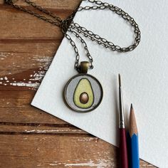 an avocado pendant is sitting on a piece of paper next to a pencil