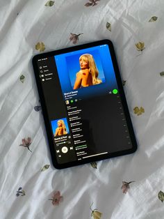 a tablet computer sitting on top of a bed covered in white sheets and gold flowers