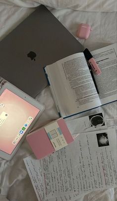 an open laptop computer sitting on top of a bed next to books and papers with writing