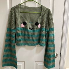 a green sweater with a face drawn on it hanging from a hanger in front of a door