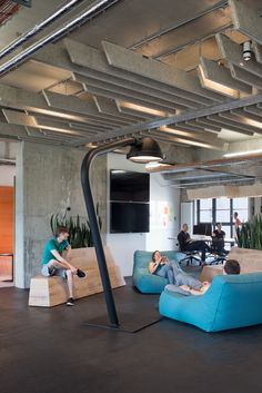 two people sitting on couches in an office with large windows and exposed ceiling beams